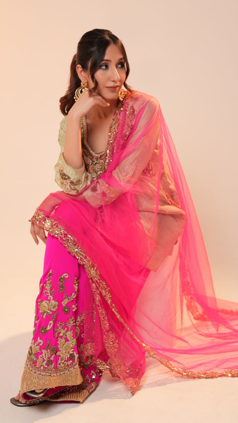 Woman wearing a pink saree with gold embroidery on a plain background
