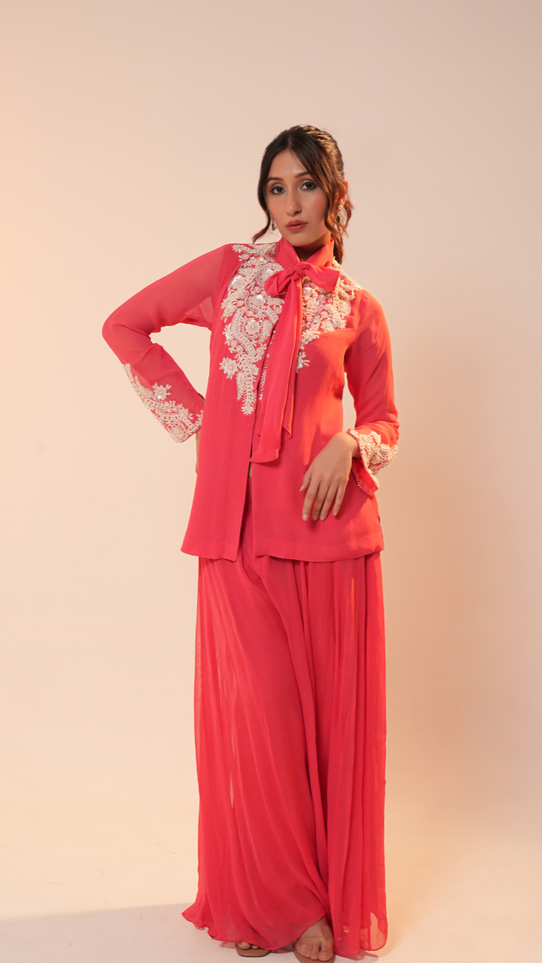 Woman wearing a coral outfit with floral embroidery on a beige background