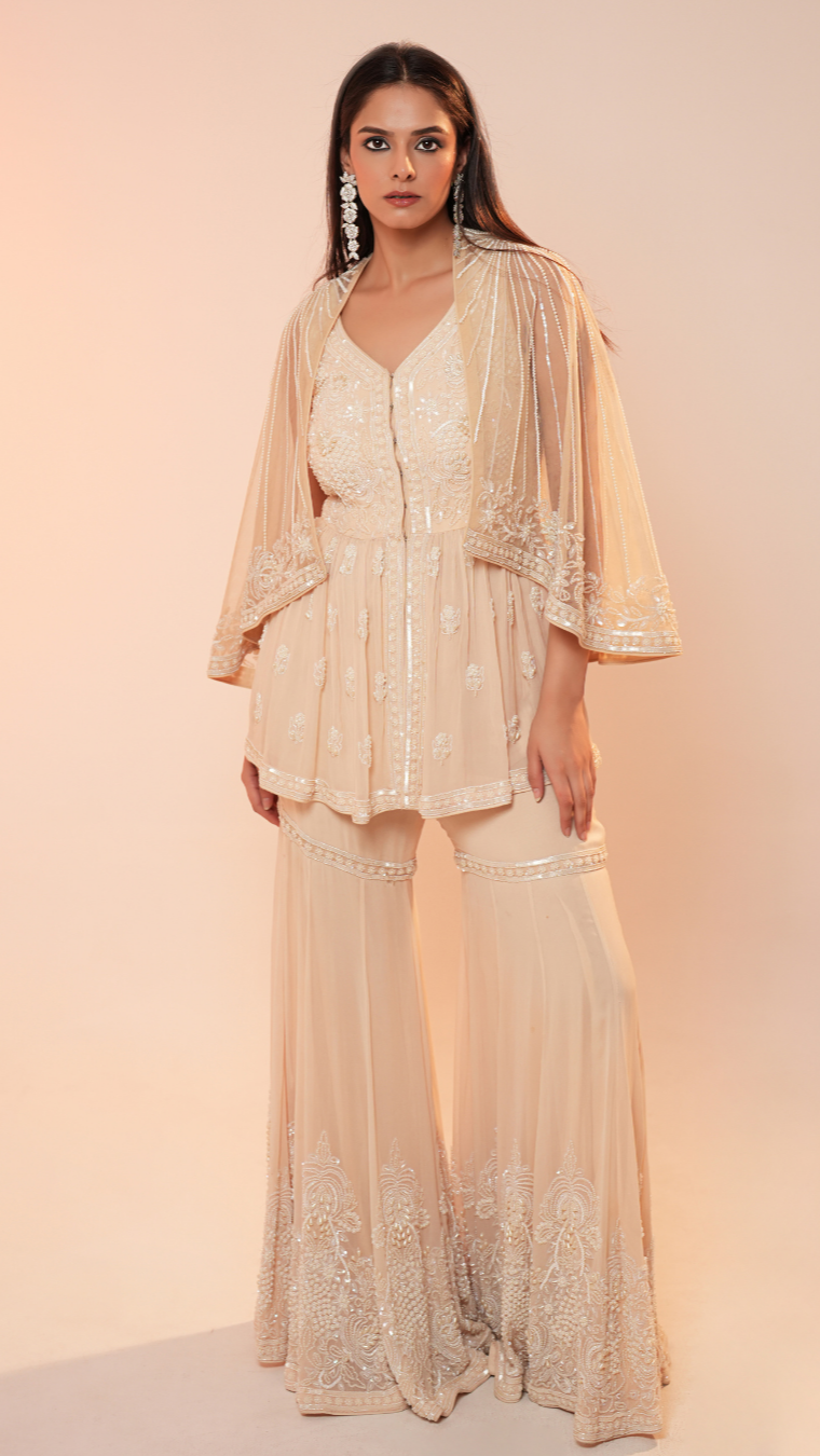Woman wearing a beige embroidered outfit with a matching jacket against a beige background