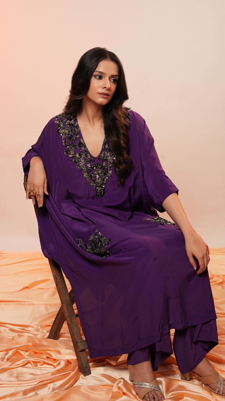 Woman wearing a purple traditional outfit with black embroidery on an orange fabric background