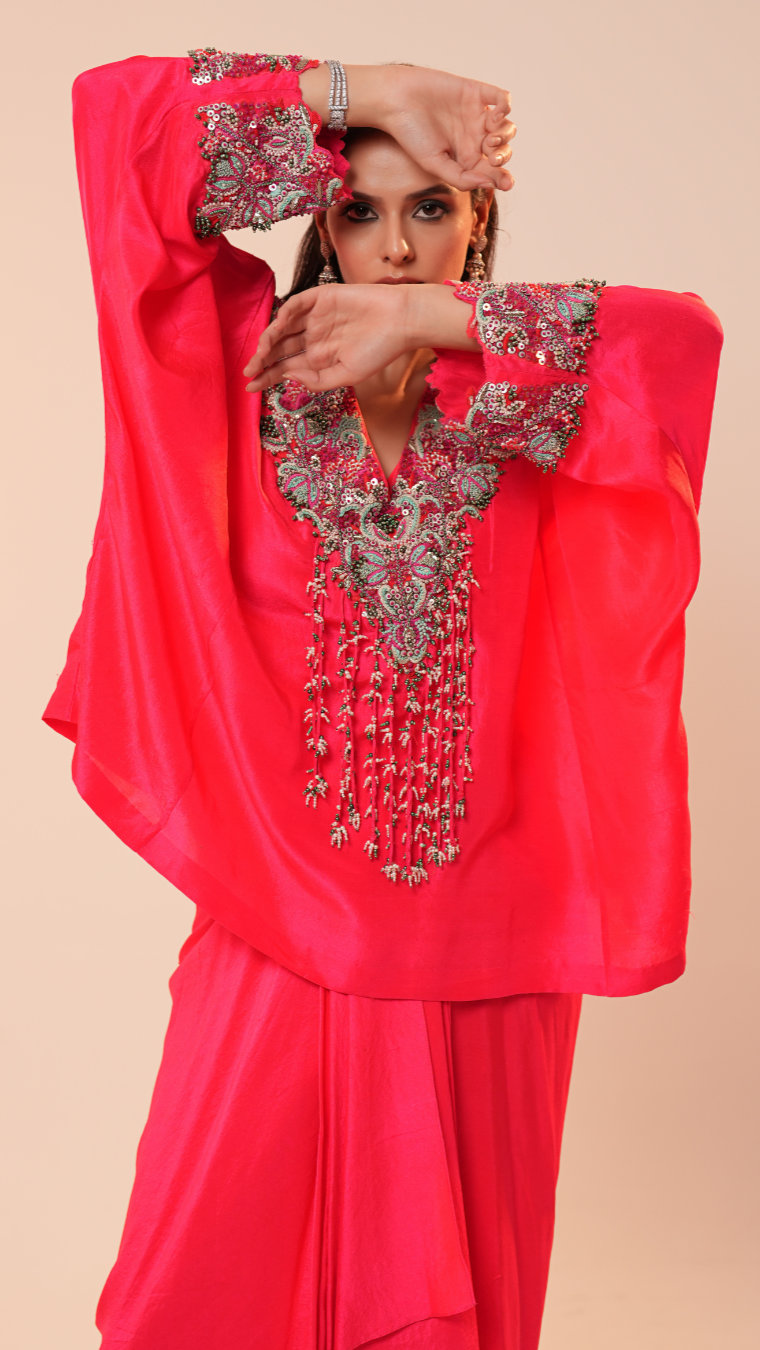 Woman wearing a bright pink traditional outfit with intricate silver embroidery on a beige background