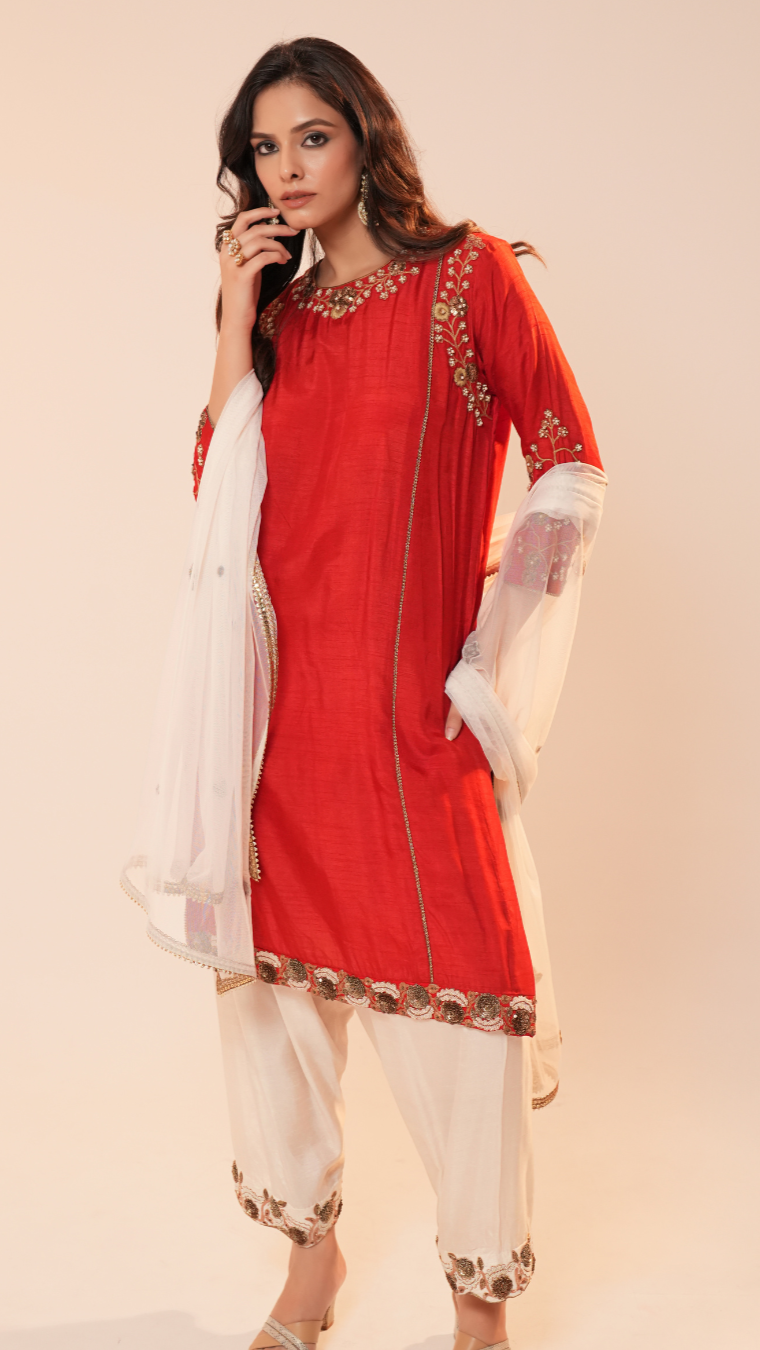 Woman wearing a red and white traditional outfit with gold embroidery on a beige background