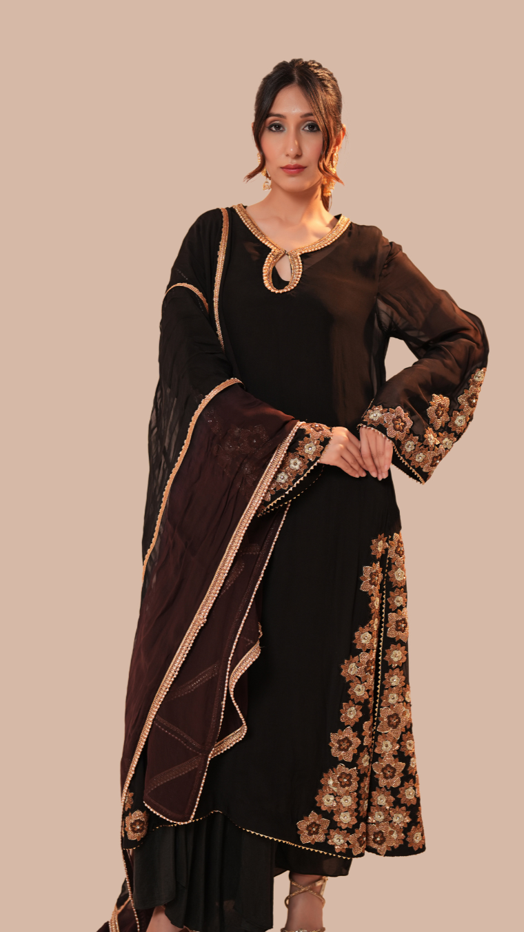 Woman wearing a black and brown traditional outfit with floral patterns on a beige background
