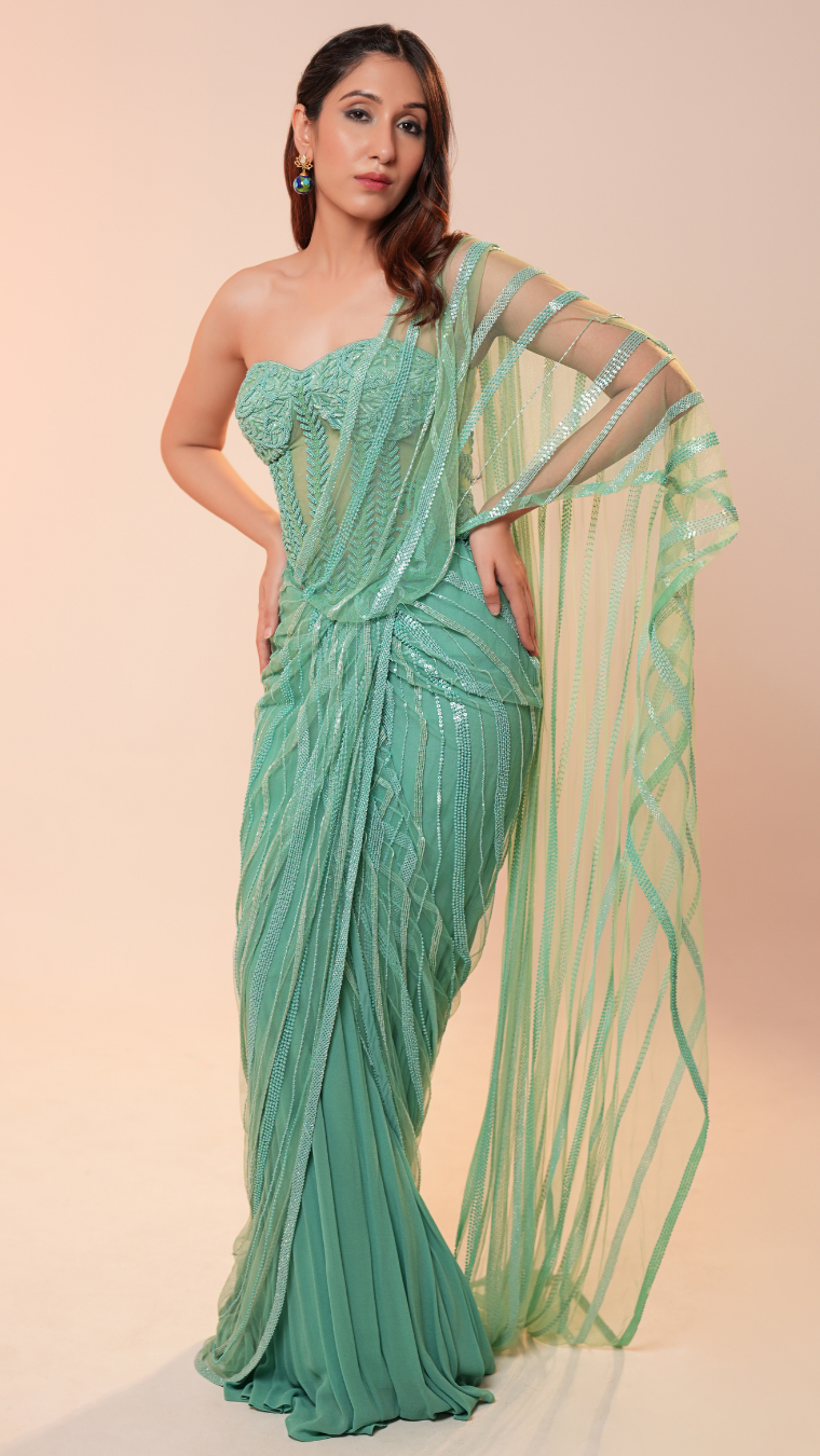 Woman wearing a green saree with a matching blouse on a beige background