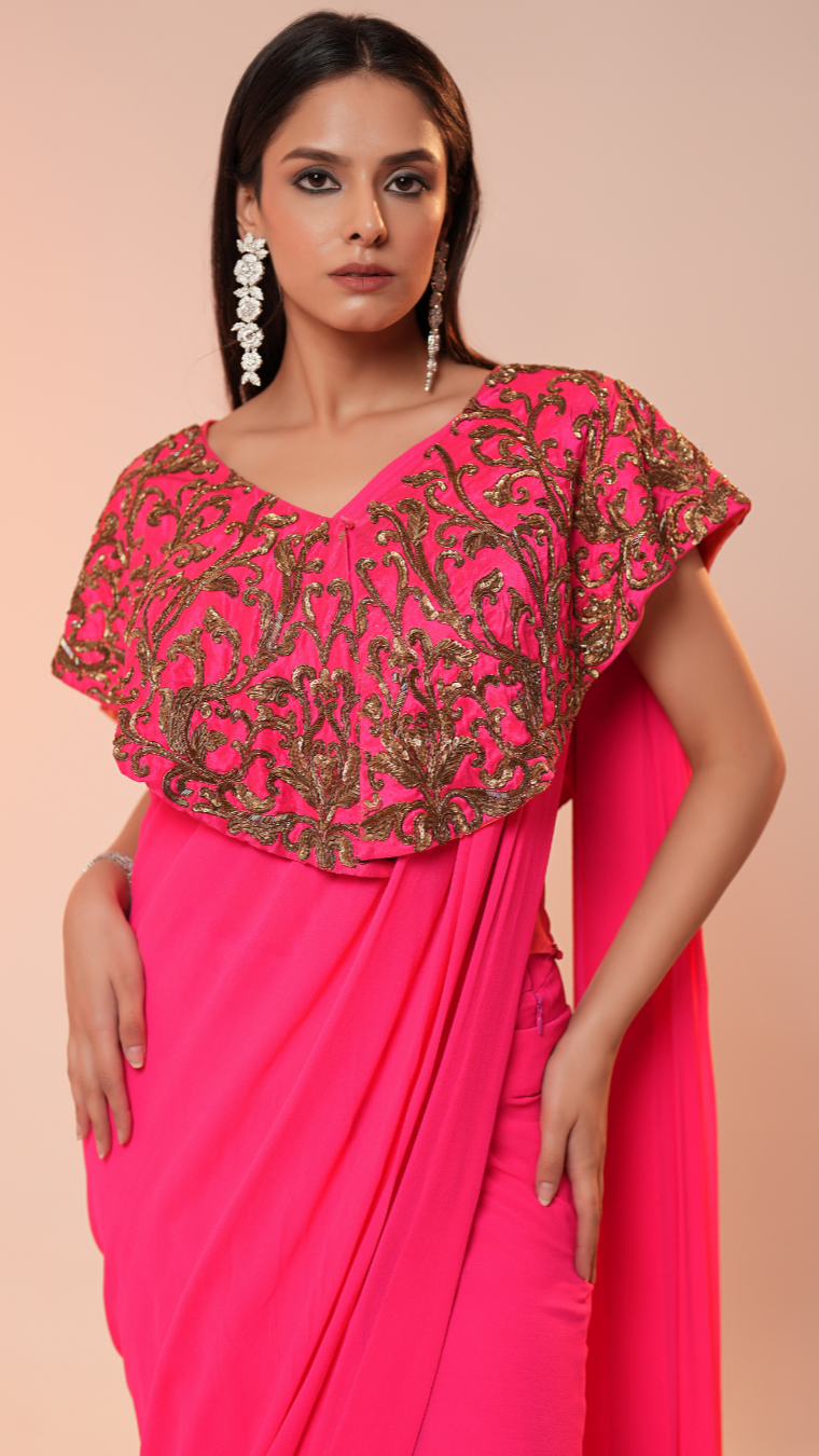 Woman wearing a bright pink saree with gold embroidery on a peach background