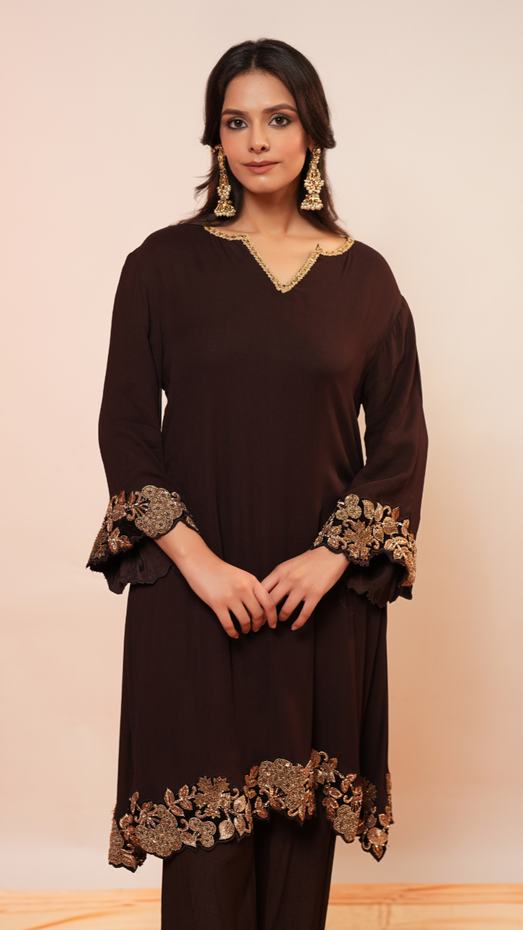 Woman wearing a brown dress with gold embroidery against a beige background