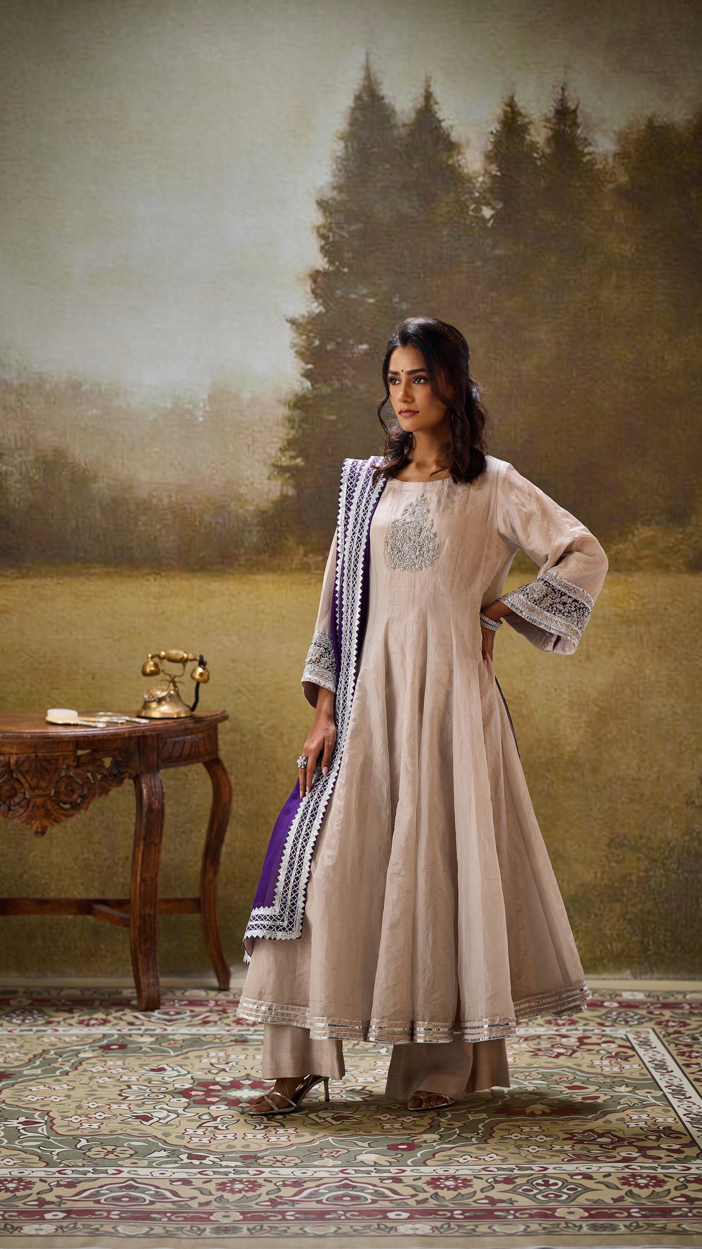 Woman in a traditional outfit standing in a room with a painting of a landscape on the wall.