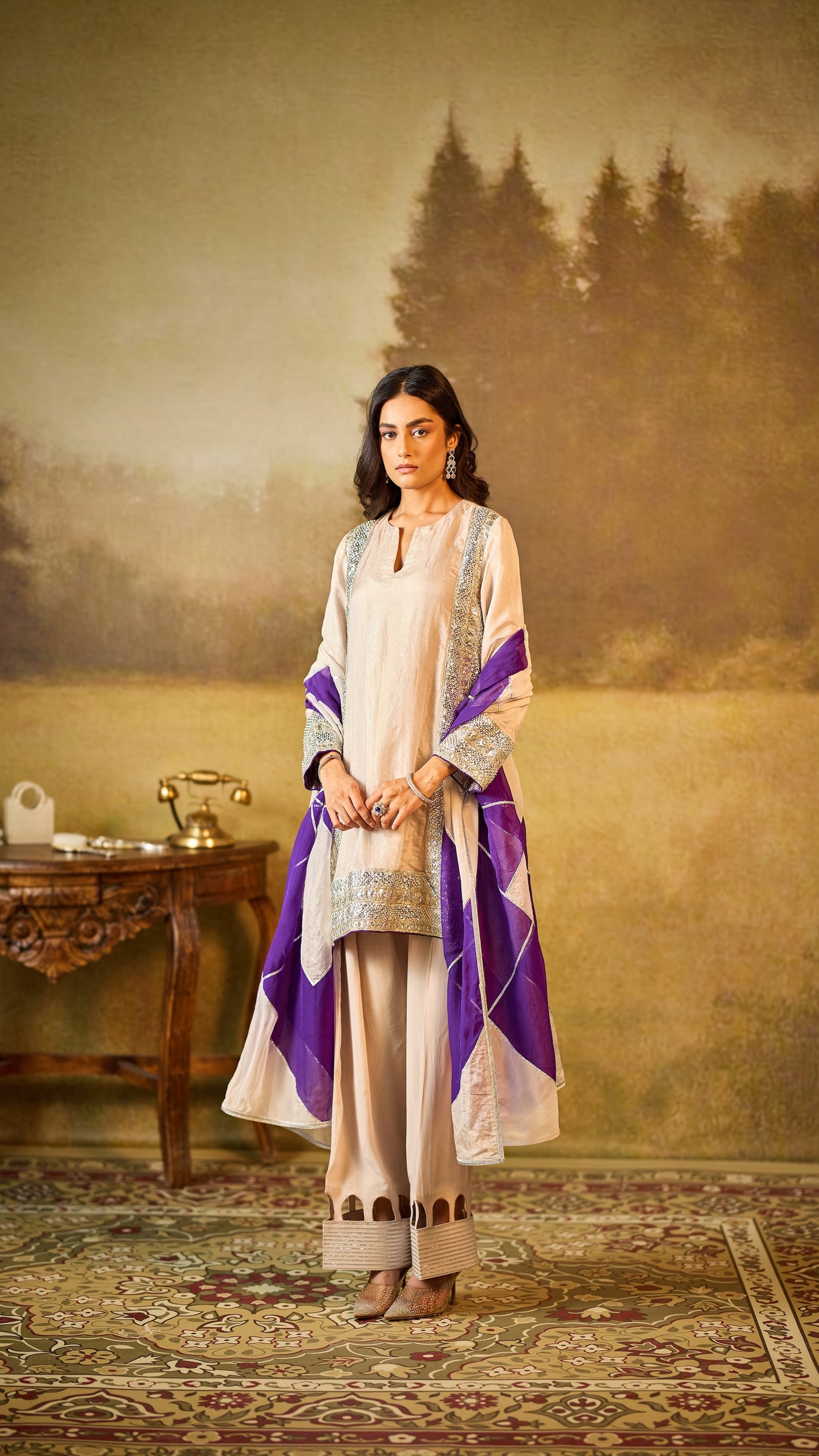 Woman in a traditional outfit standing in a room with a painting of trees in the background