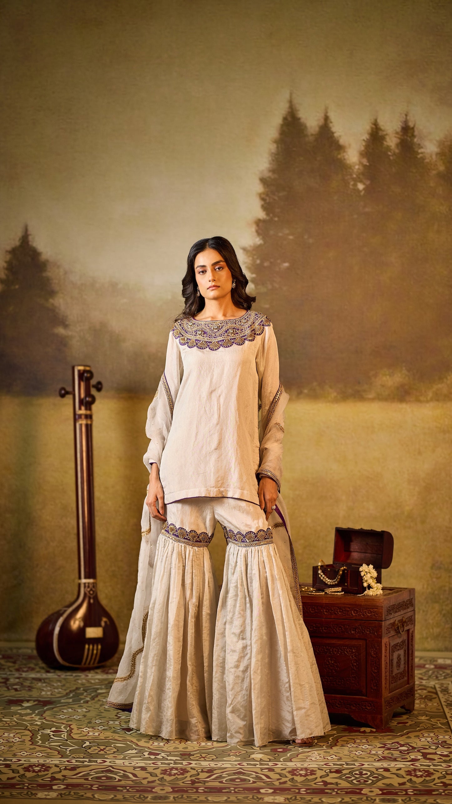 Woman in traditional outfit with a musical instrument and suitcase in a scenic setting