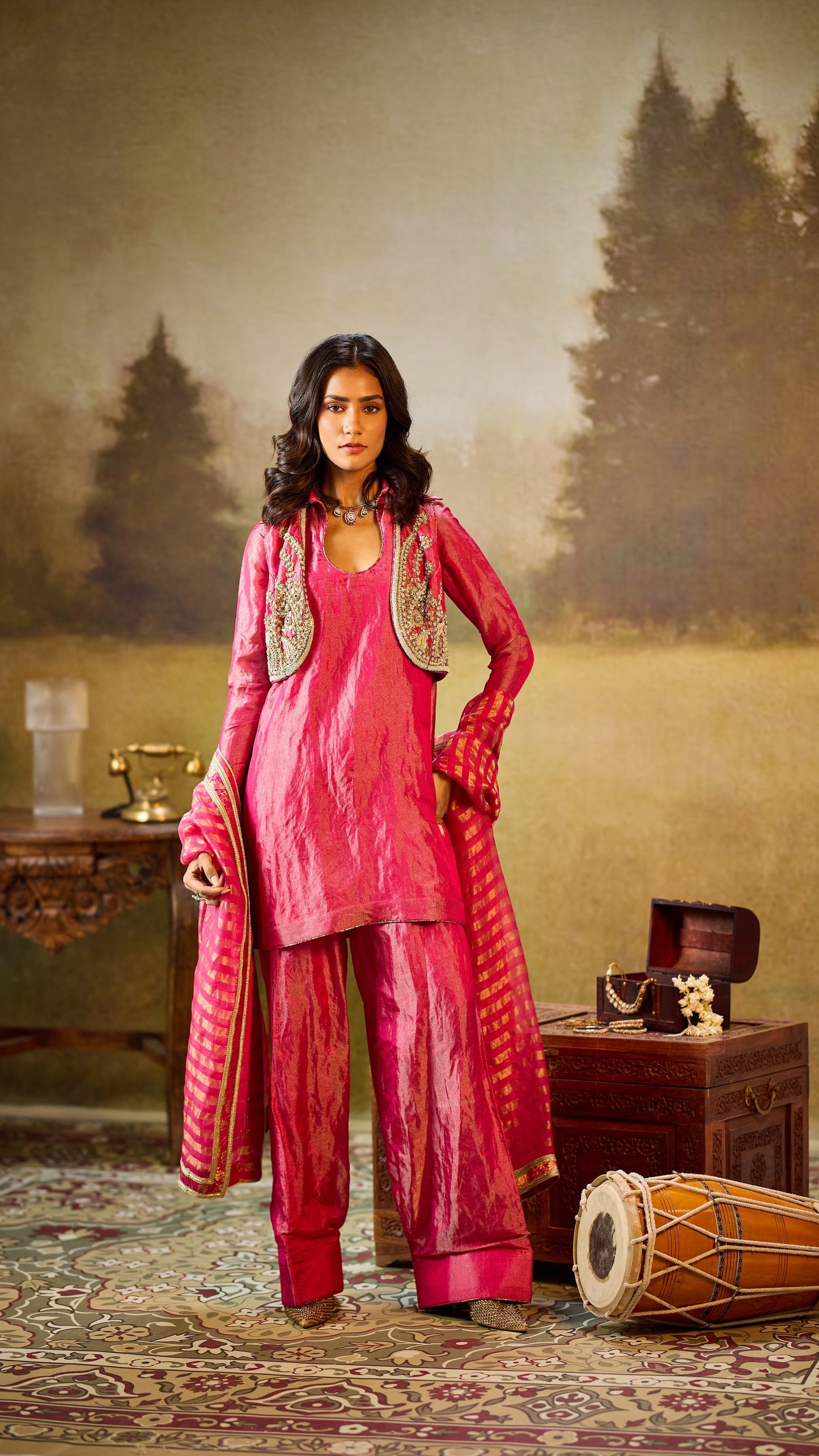 Woman in a pink traditional outfit standing in a decorated room with trees in the background