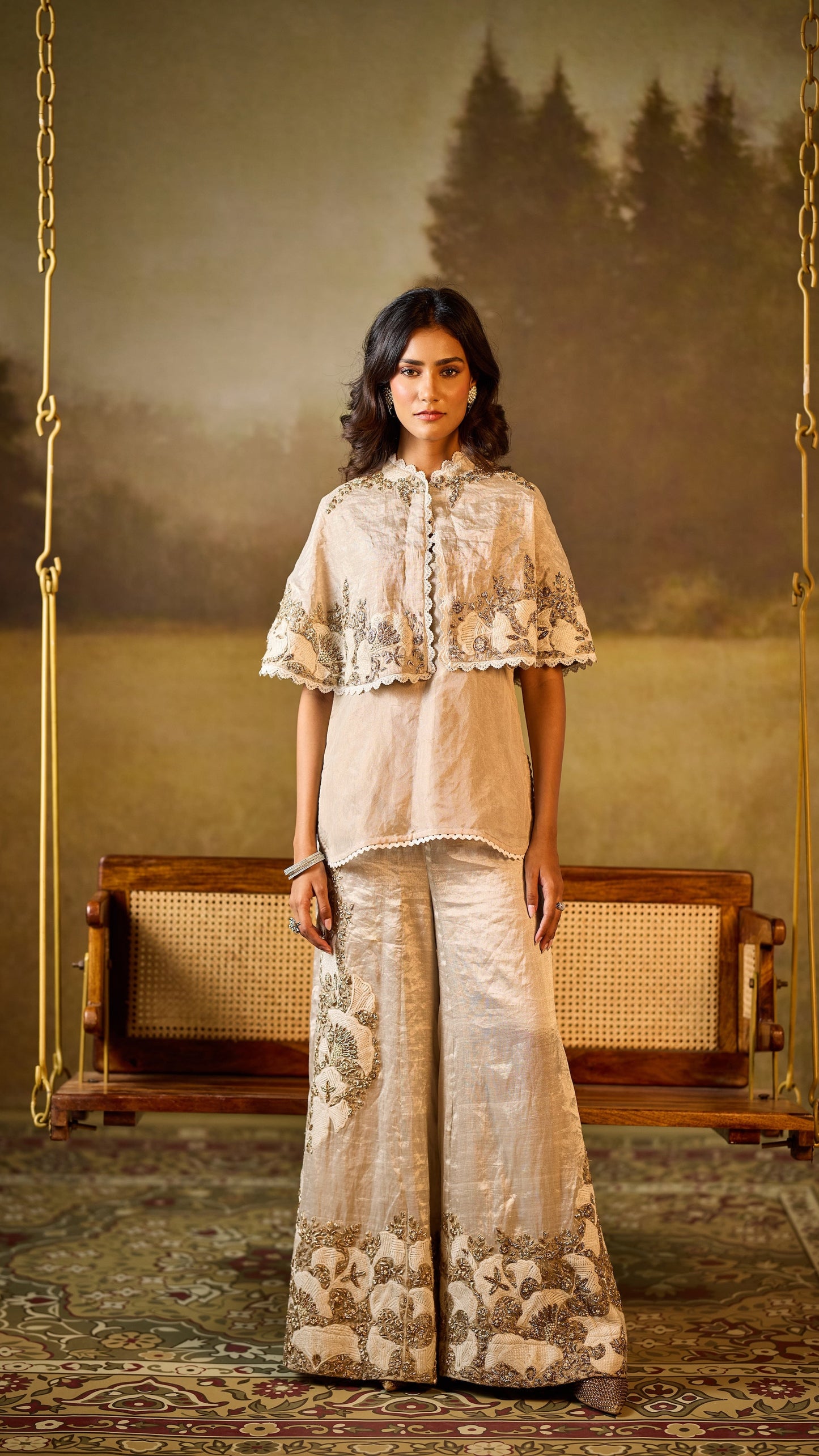 Woman in a traditional embroidered outfit standing in a room with a swing and painting.