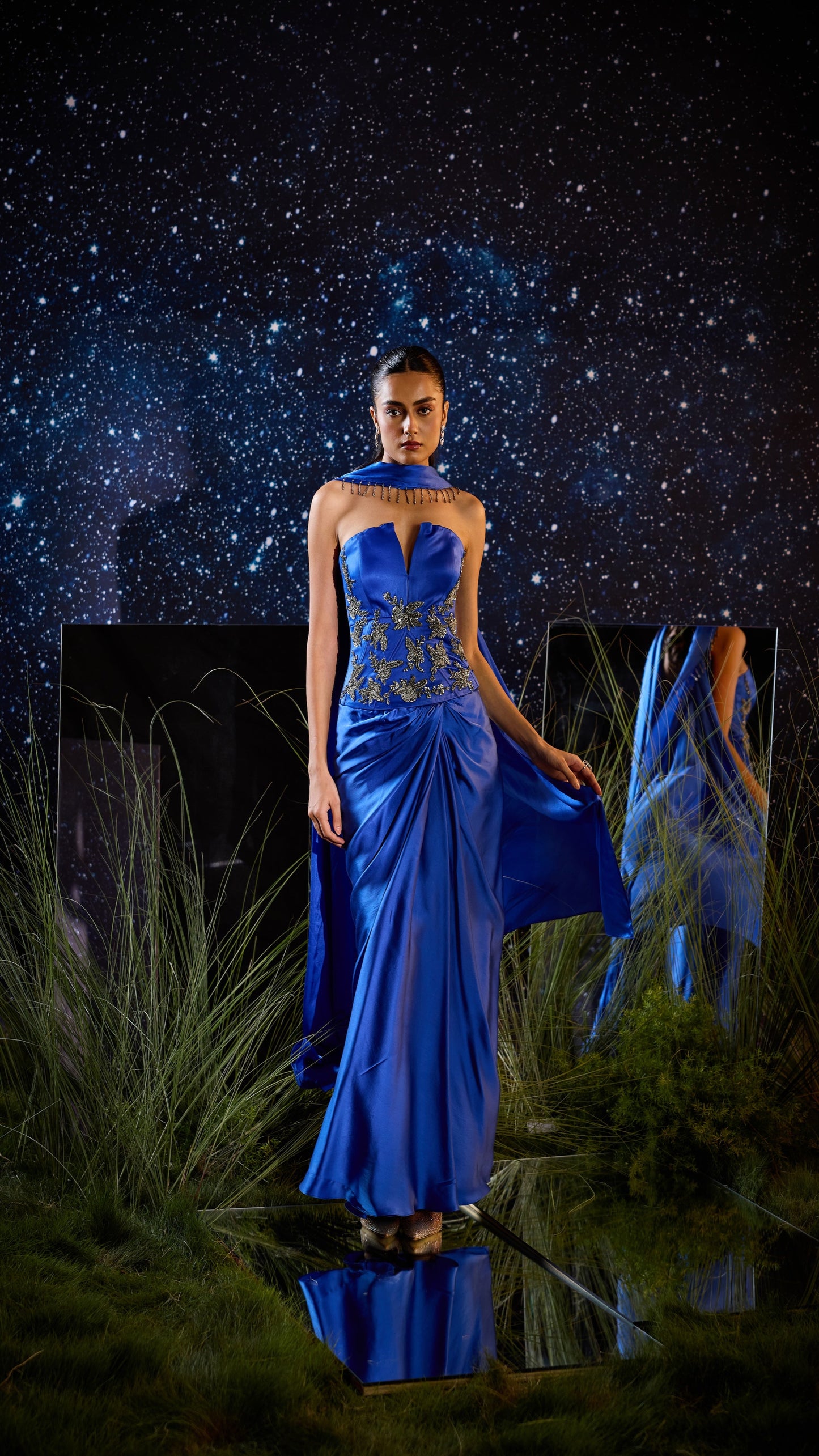 Woman in a blue evening gown standing against a starry night sky.