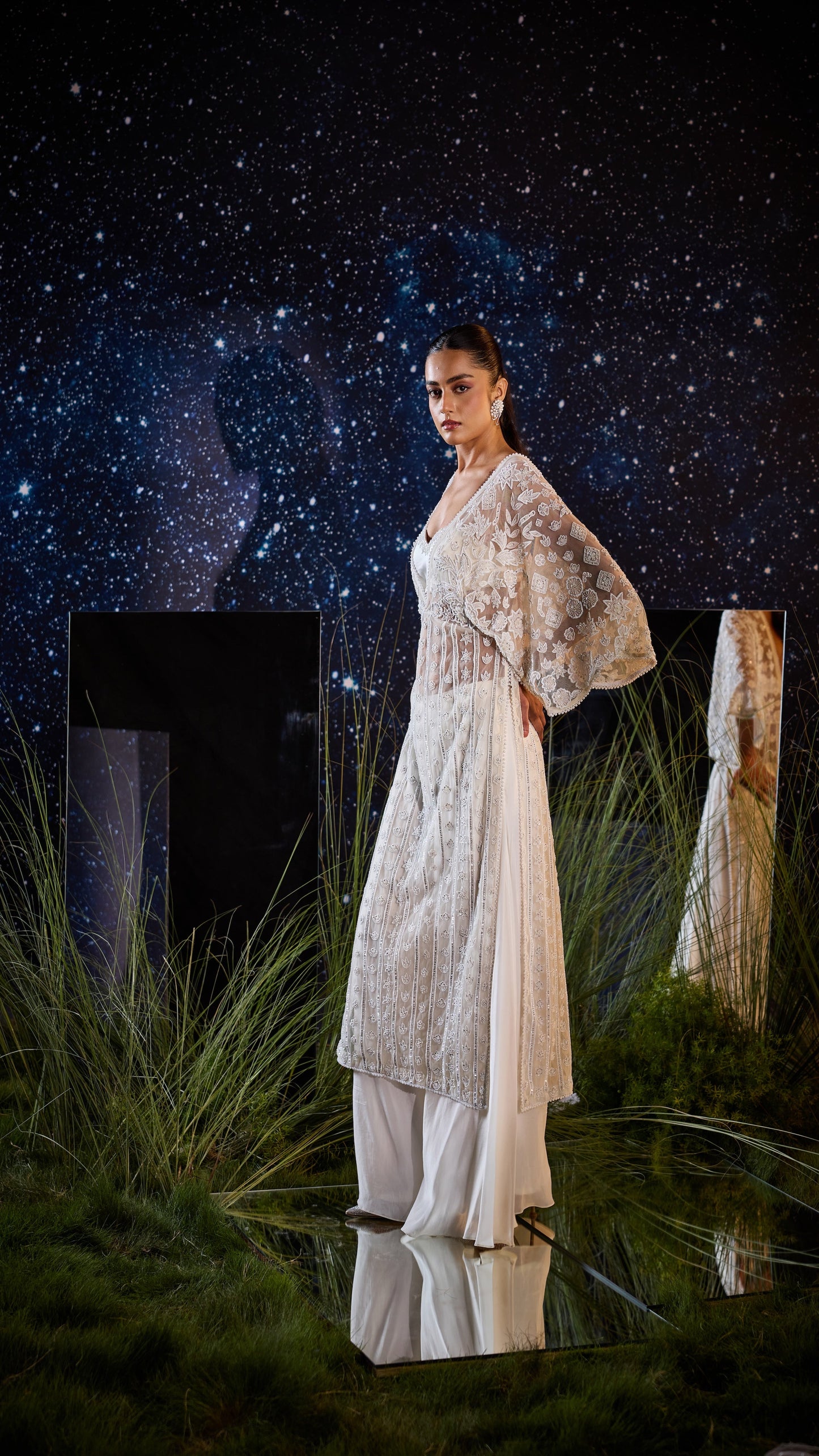 Woman in a white and beige outfit standing against a starry night sky.