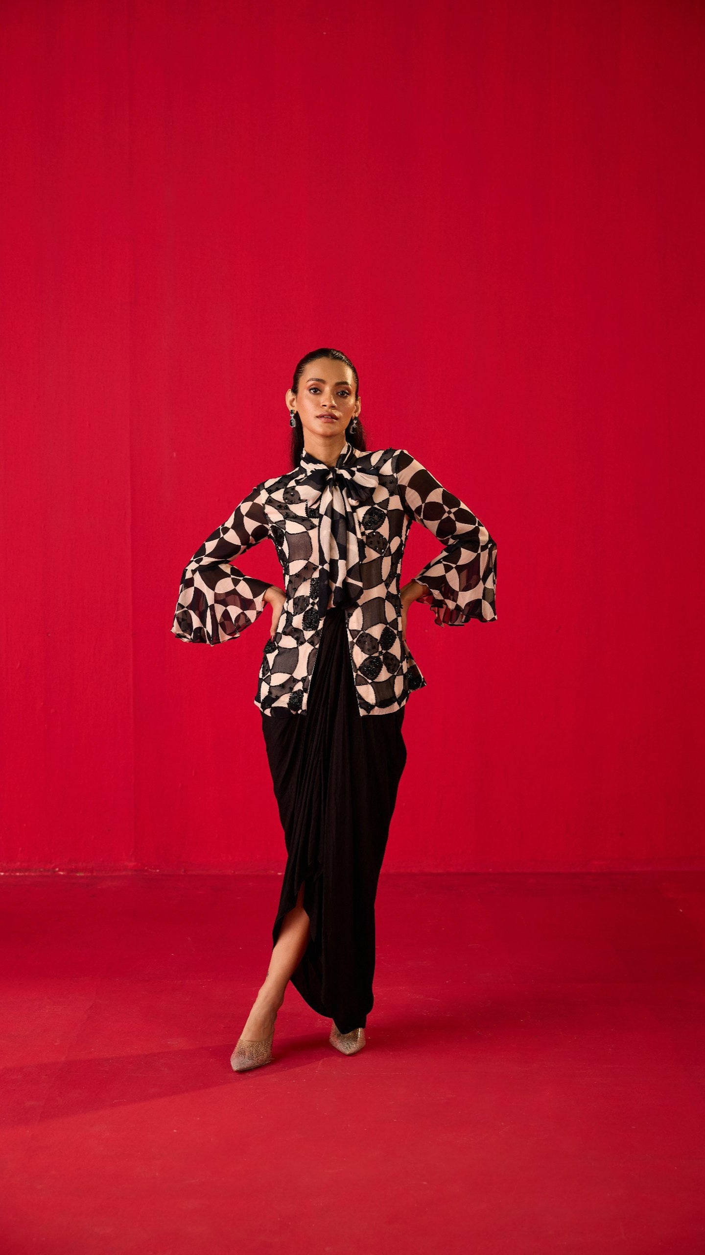 A person wearing a traditional dance dress with a floral pattern on the upper half and solid color on the lower half, posing against a red backdrop.