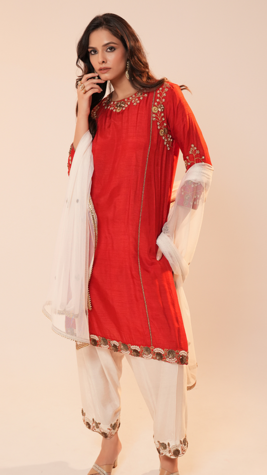 Woman wearing a red and white traditional outfit with gold embroidery on a beige background
