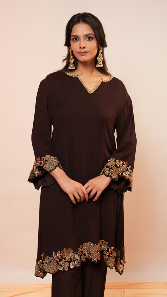 Woman wearing a brown dress with gold embroidery against a beige background